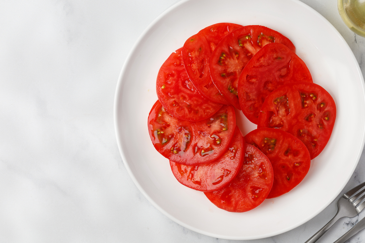 Slices of tomatoes are stacked on a white plate in a circle. Top view, copy space, mock up. Empty salad.