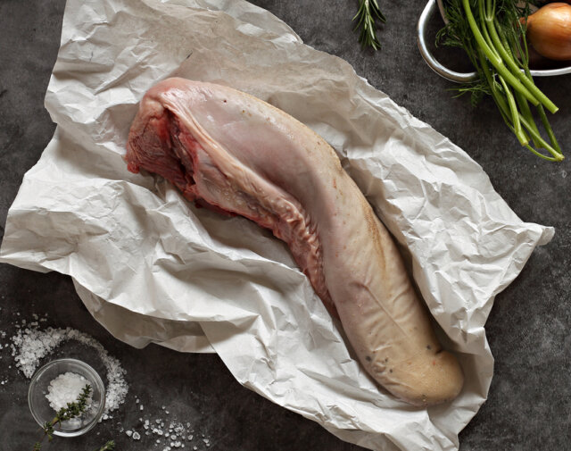 Raw beef tongue with vegetables and herbs on dark background.