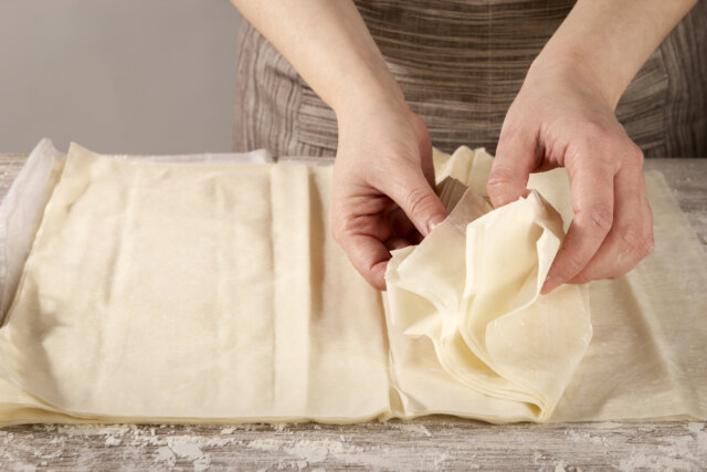 Woman separating phyllo pasta leaves to cook a healthy recipe. Concept of healthy home cooking.